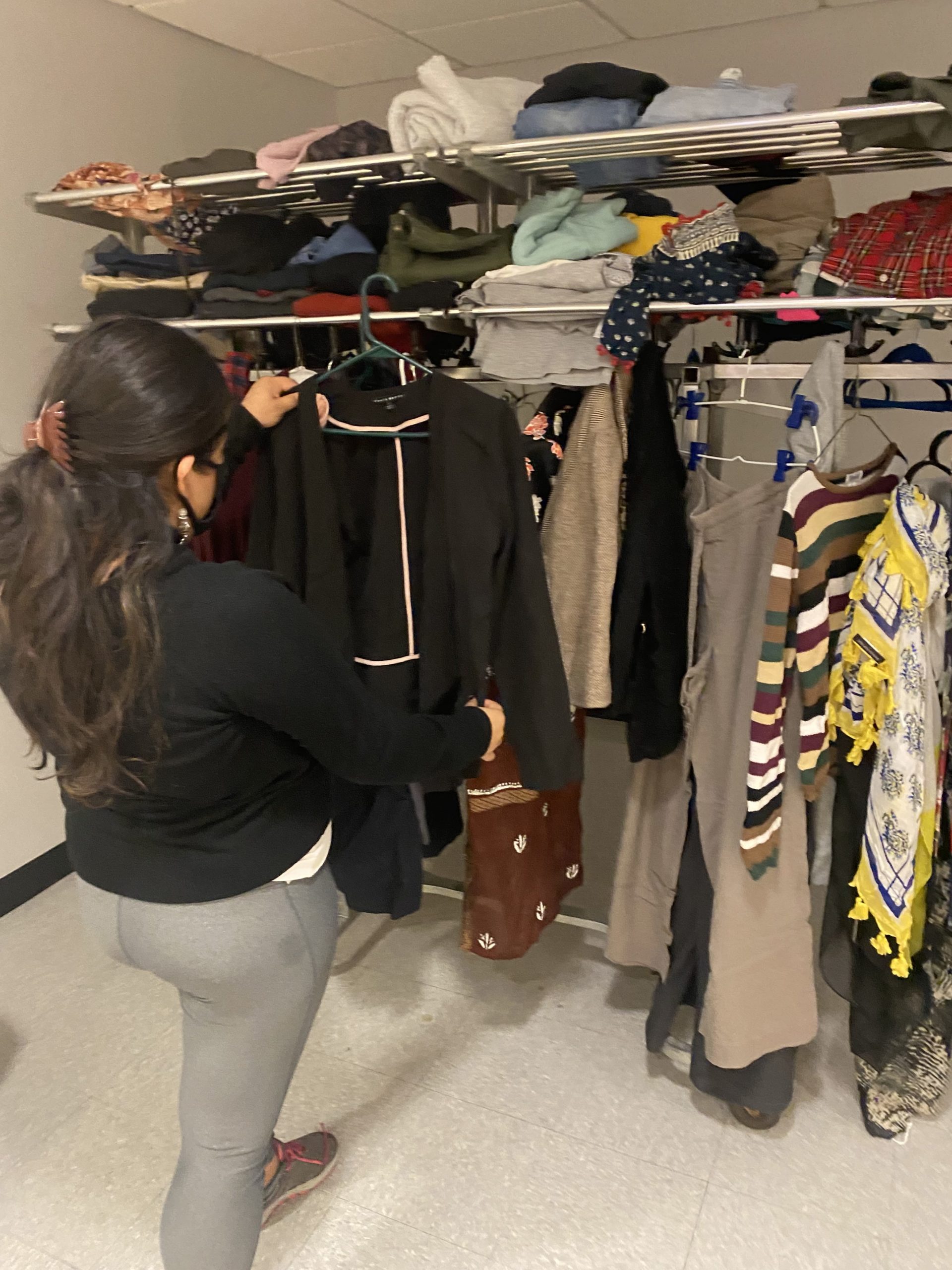 A clothing swap participant examines an item in front of a rack of clothing