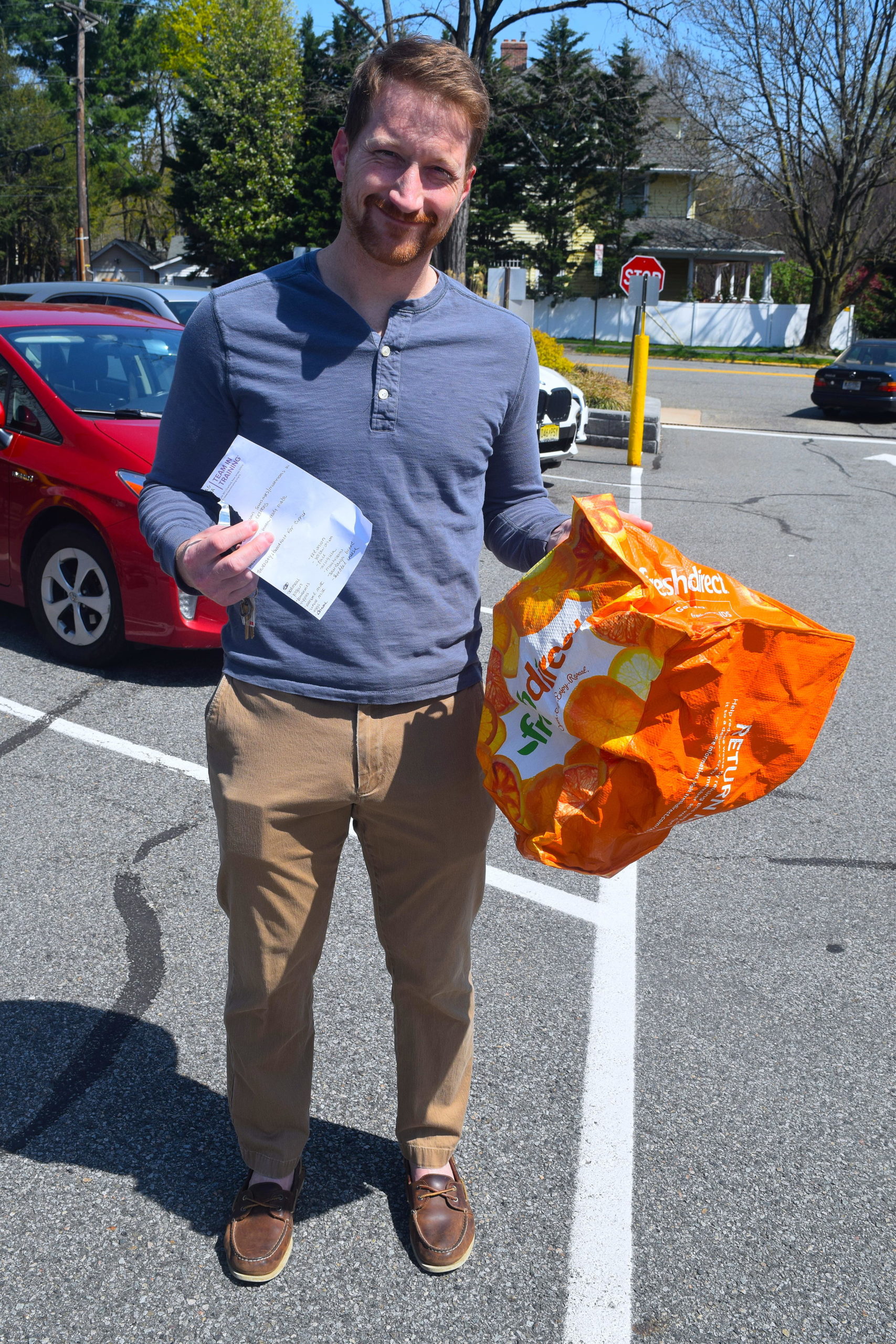 A man holds a reusable shopping bag in a parking lot