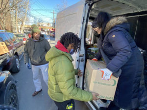 Three people in cold-weather gear are loading a box marked "eggs" on or off a van