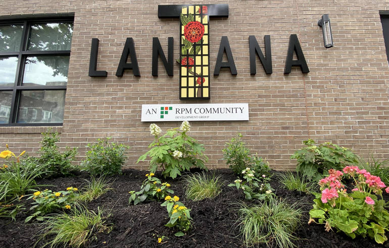"Lantana" is spelled out on the exterior of a building, with landscaping plants in the foreground
