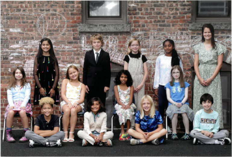 Twelve children and an adult pose formally in front of a brick wall