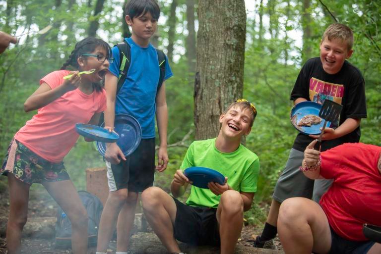 A few kids holding frisbees laugh