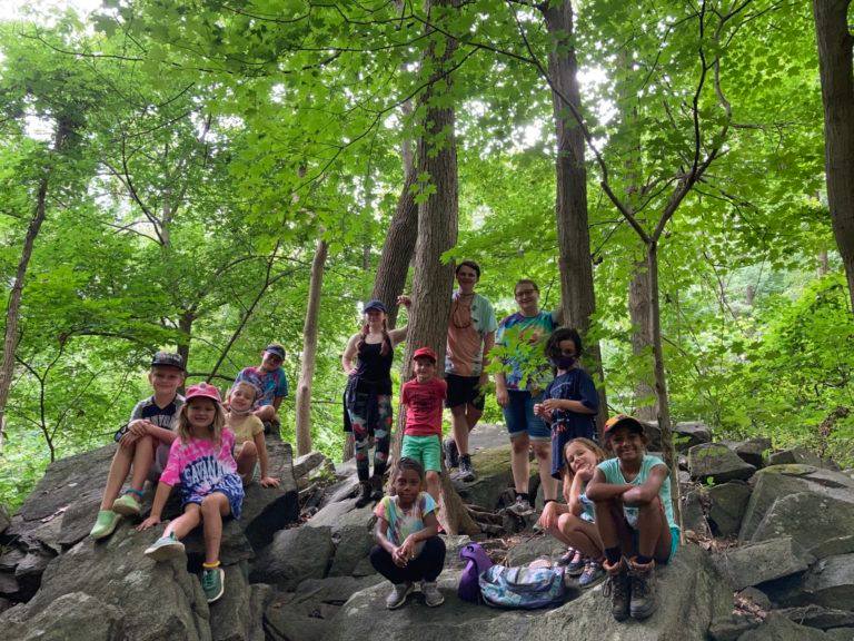 Nine children and three adults pose on a huge rocky formation in a wooded area