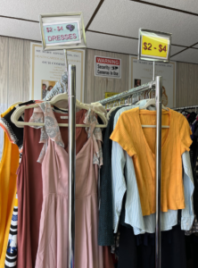 Two racks of clothing bear the signs "$2-$4 DRESSES" and "$2-$4"