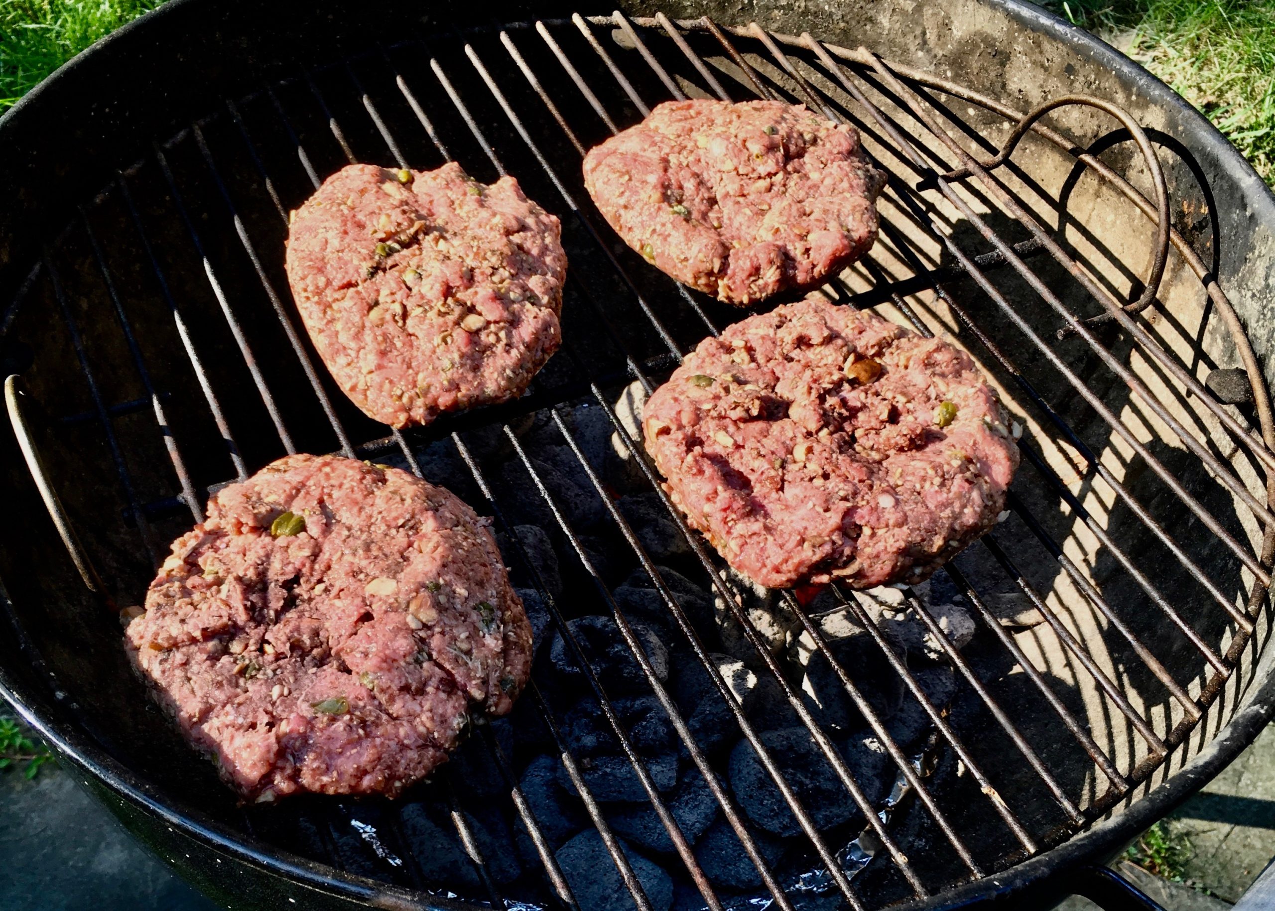 Four raw burgers on a grill