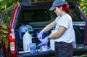 A person works with various containers arrayed in the open back of a vehicle