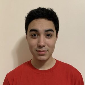 A medium tone, young man wearing a red shirt. He has short dark hair.