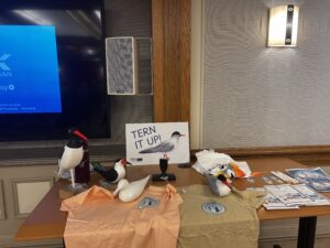 Replica birds rest on a table. Behind them is a sign that reads tern it up.