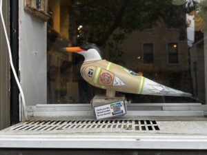 A statue of a bird with an orange beak and white and black head feathers rests on a perch in front of a window