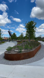 Concrete pathways wine through green spaces. In the background is a large metallic structure